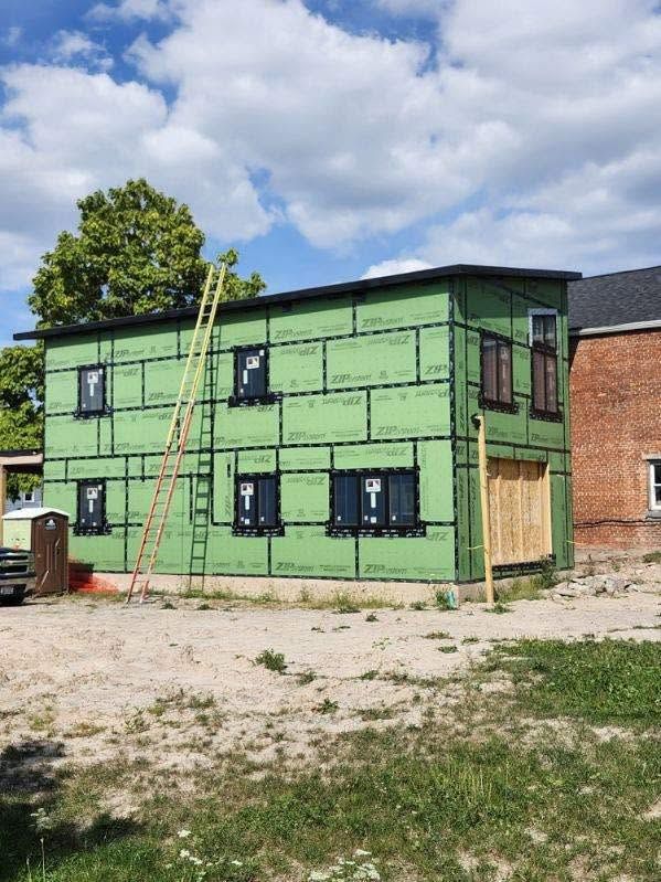 Green two-story house under construction with black-trimmed windows and a ladder against the wall