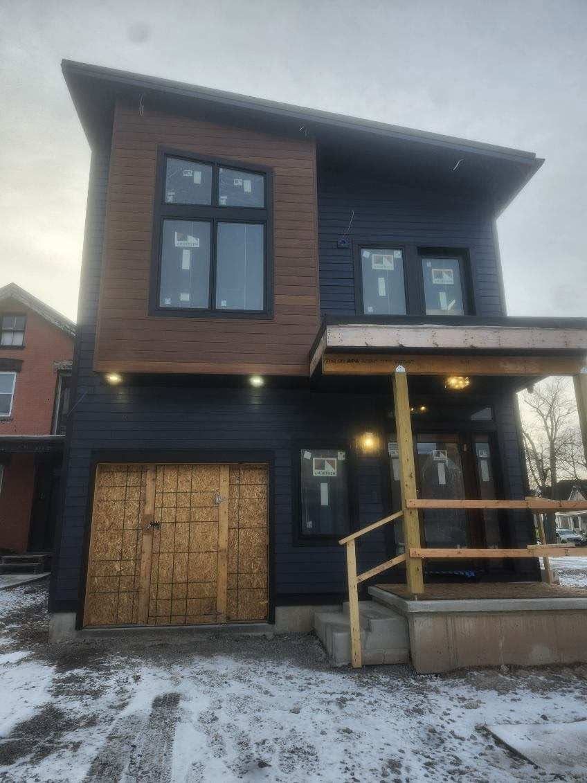 Two-story brown house with a garage, porch, and snow-covered yard at dusk