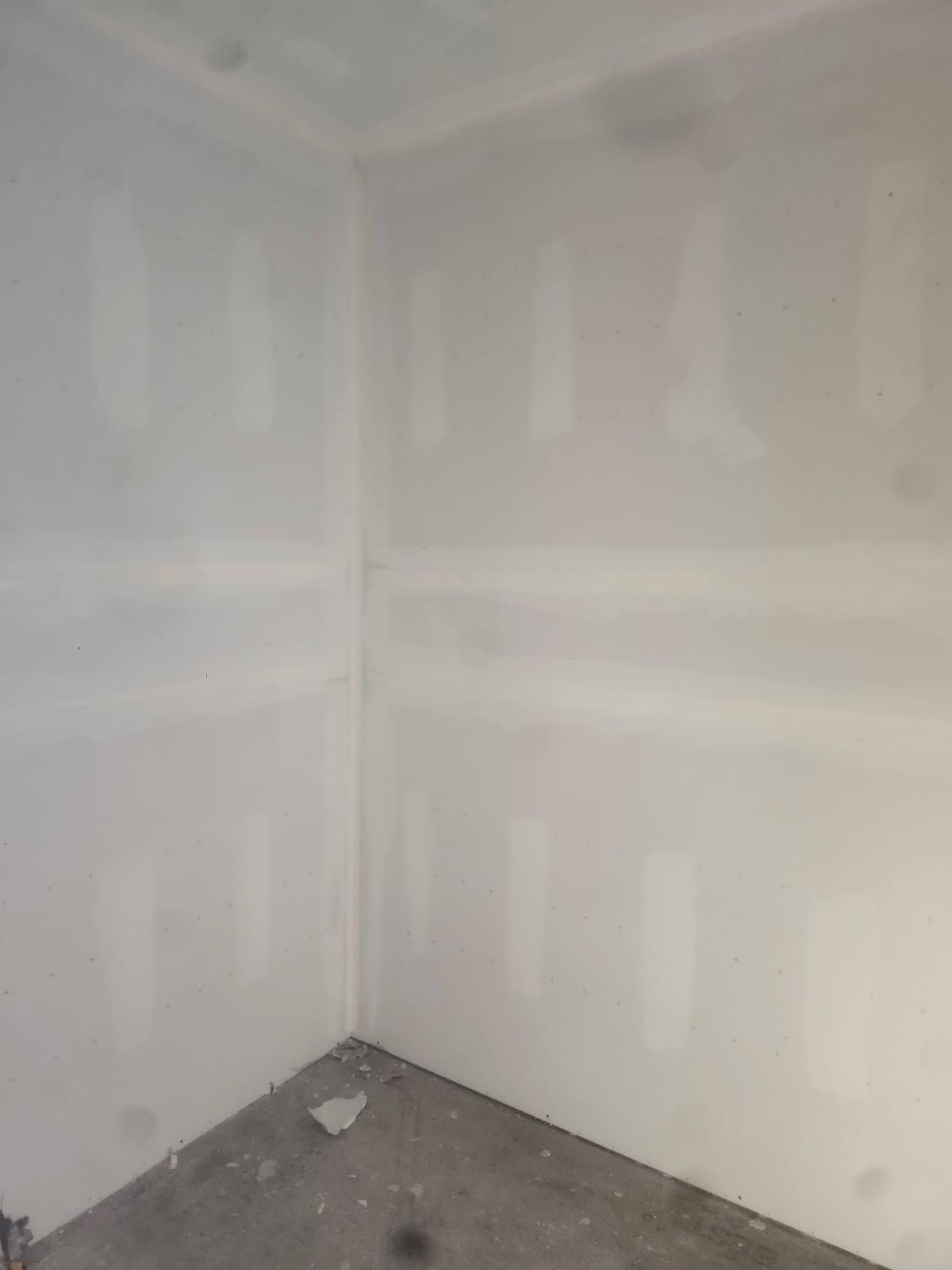 Empty drywall corner with white taped seams and unfinished gray floor.