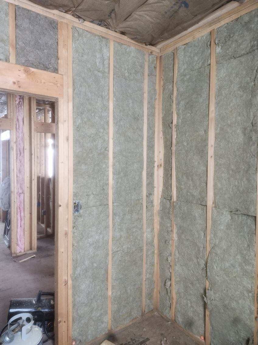 Insulated wall framing inside an unfinished room, with exposed studs and a doorway opening.