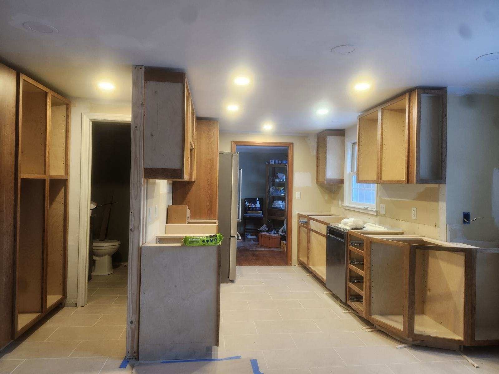 Empty kitchen interior with wood cabinets, beige counters, and central island under recessed lights