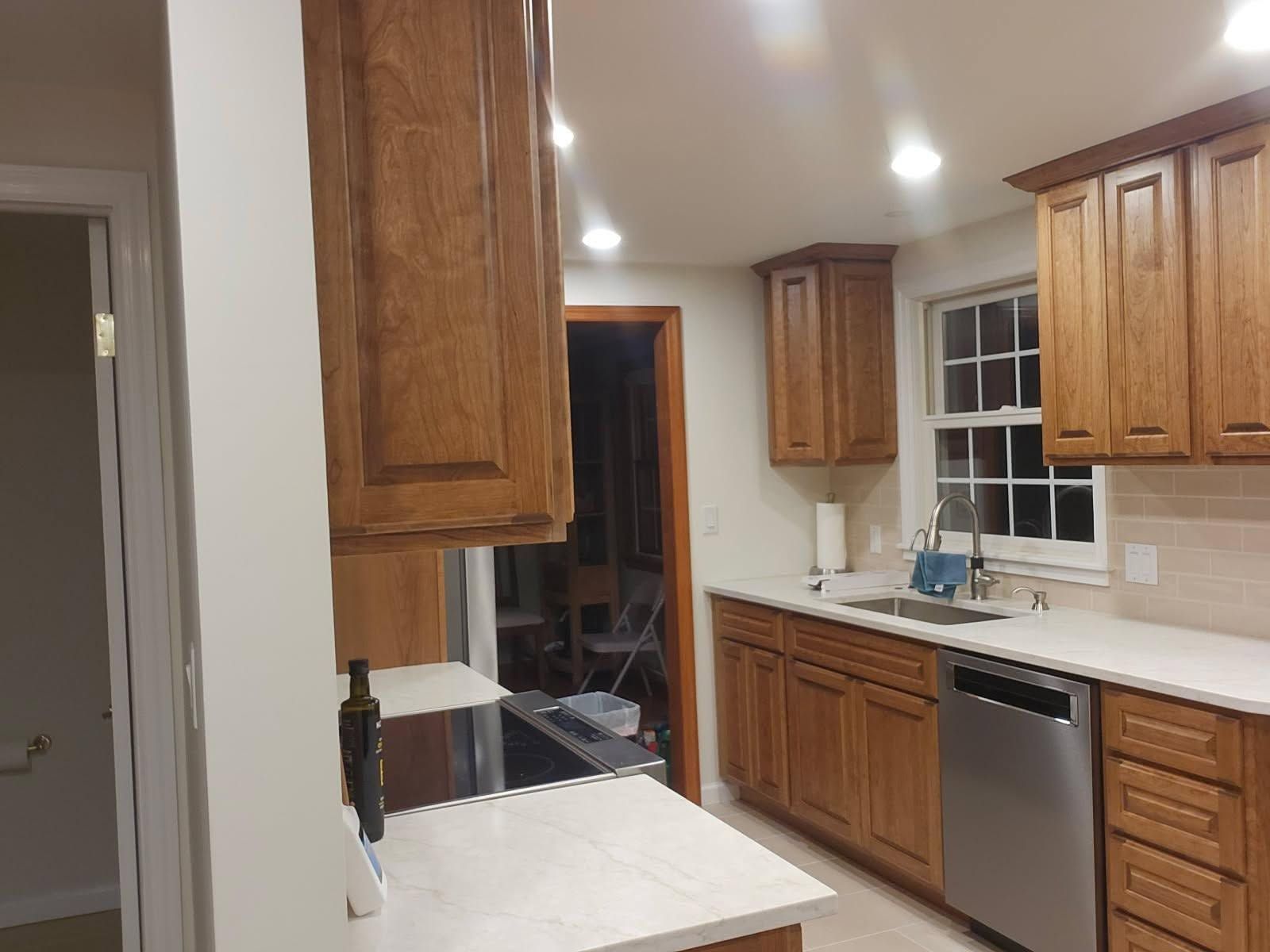 Wooden kitchen with white countertops, recessed lights, dishwasher, and open doorway to a dark room