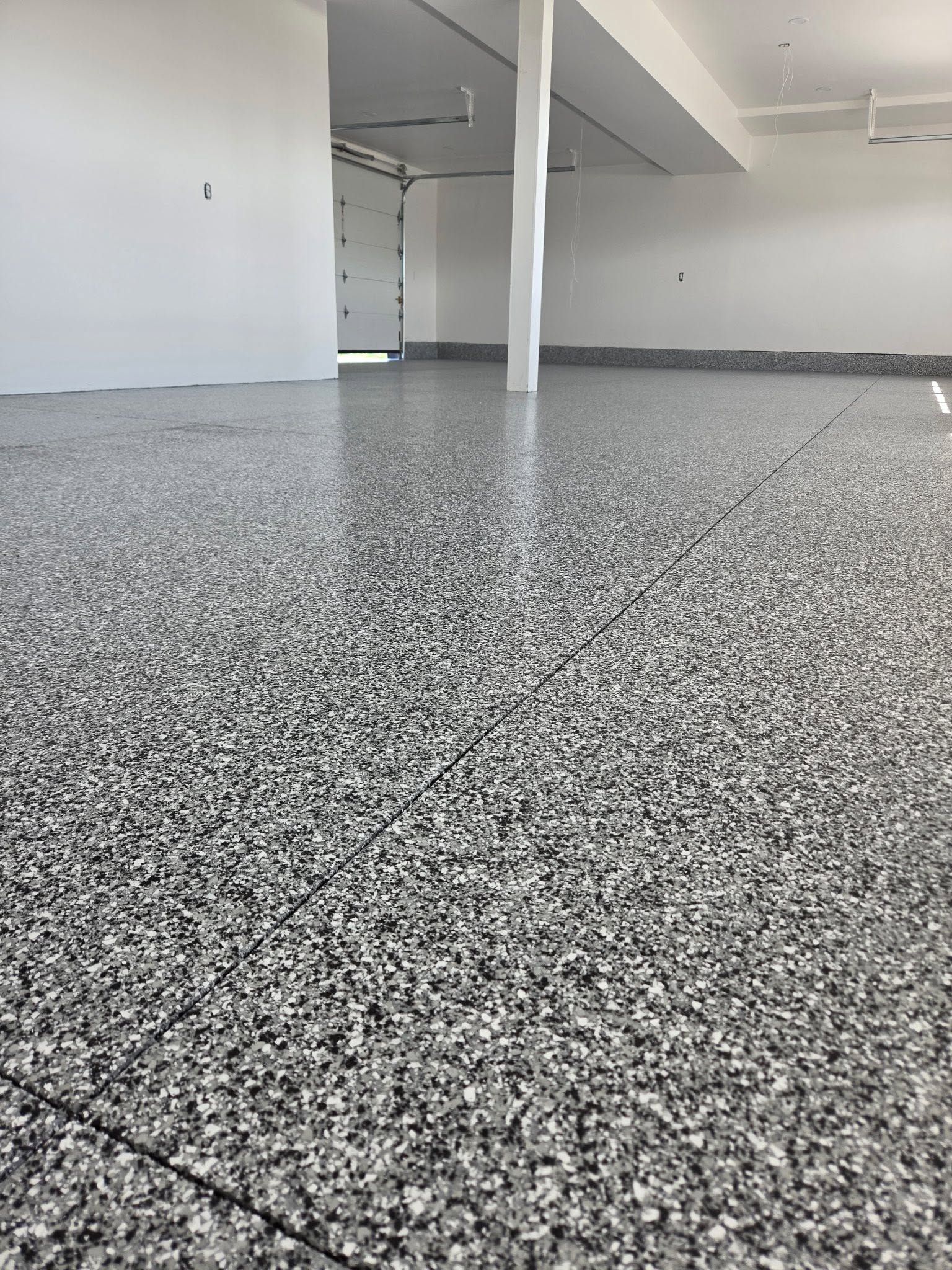 Empty room with speckled gray epoxy floor, white walls, and a central support column