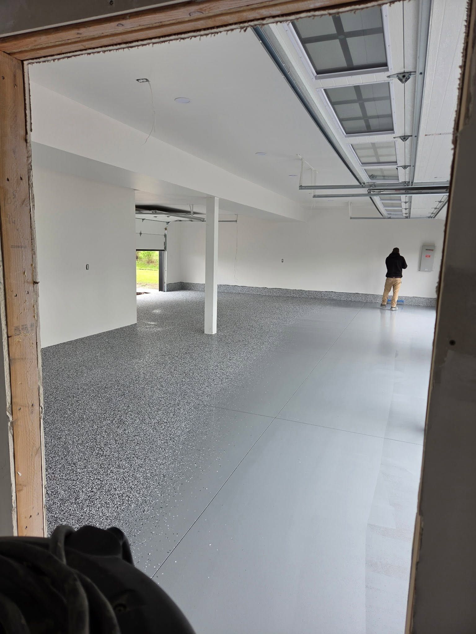 Partially finished garage with gravel, smooth floor, and a person near the back wall