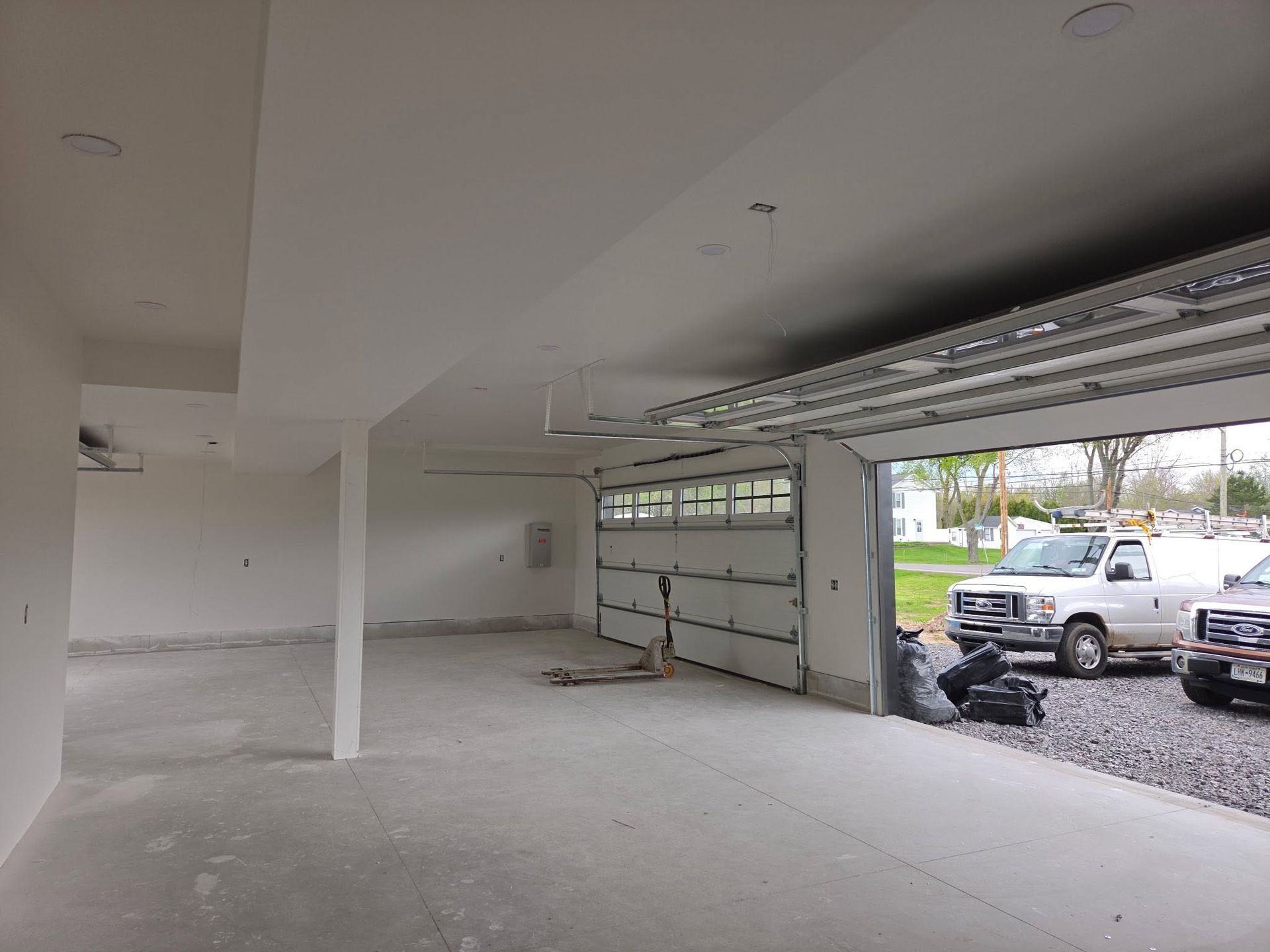 Empty unfinished garage with open door, concrete floor, and parked truck outside