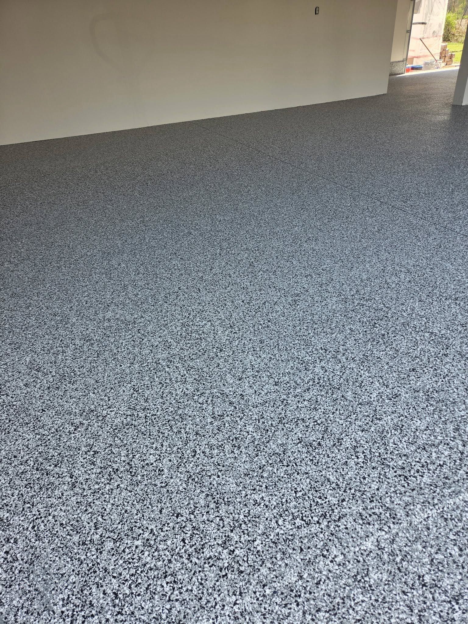 Speckled gray floor in an unfinished indoor space with a doorway opening to the outside