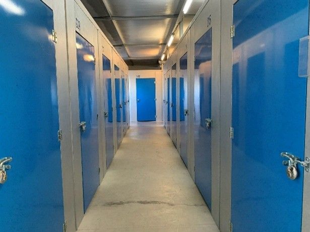 A hallway with multiple blue storage unit doors secured with padlocks inside a storage facility A hallway with multiple blue storage unit doors secured with padlocks inside a storage facility