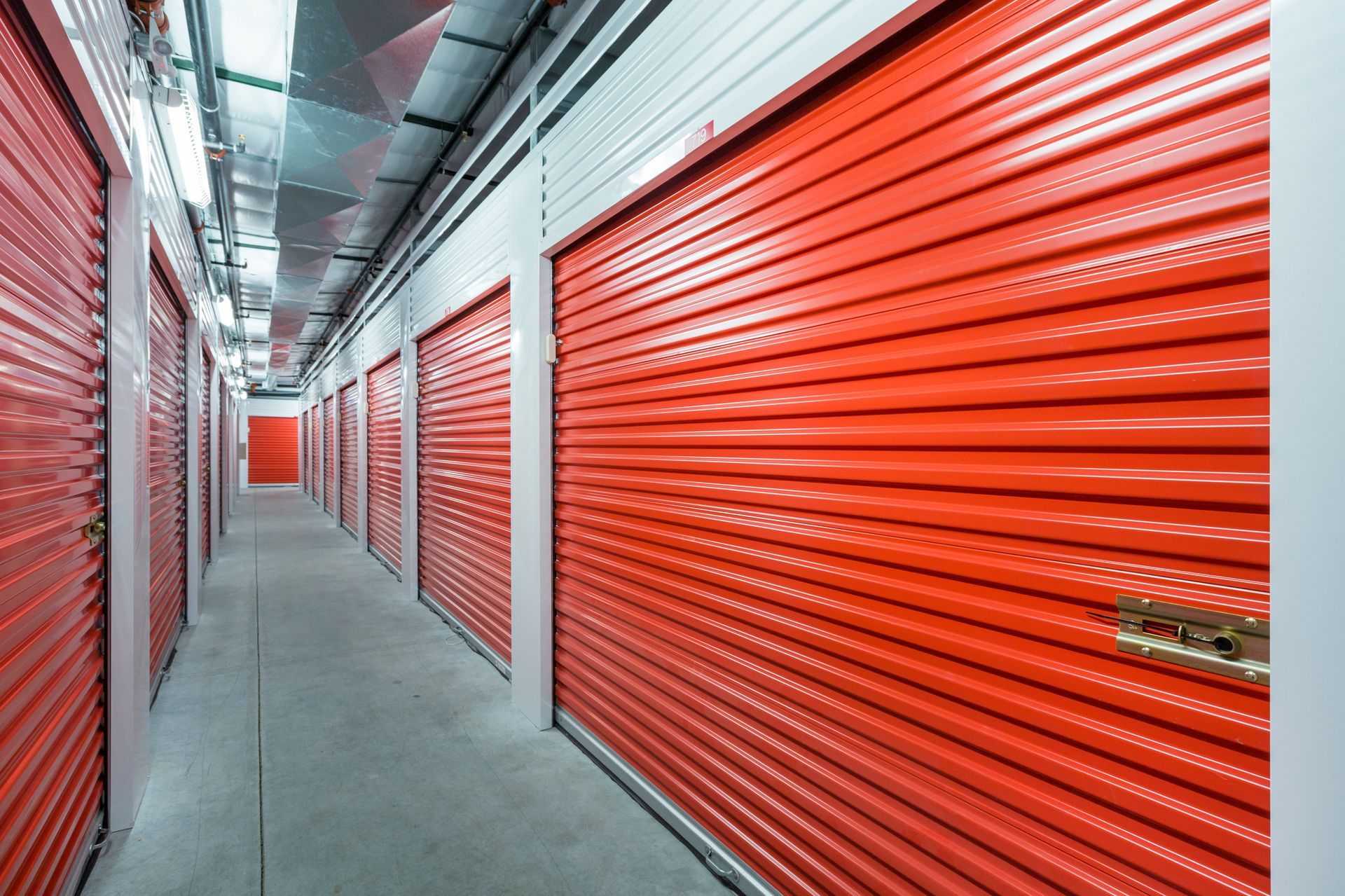 Clean indoor self-storage hallway lined with bright orange metal roll-up doors throughout the space