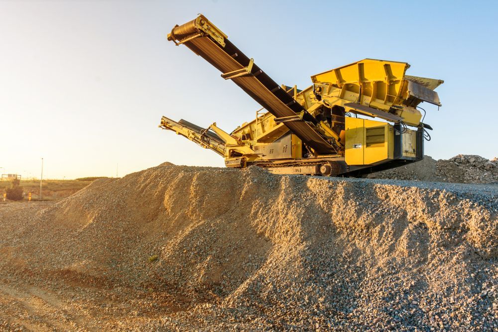 Yellow Rock Crusher on a Pile of Gravel, With a Conveyor Belt Against a Bright Sky — Waite Diesel Service in Douglas, QLD