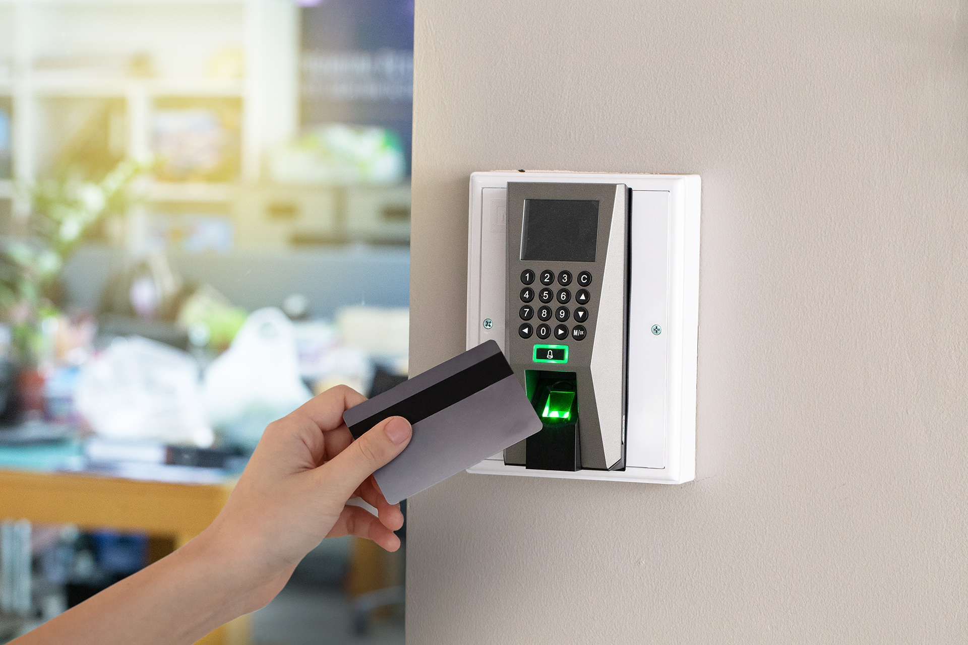 Hand holding a card near a wall-mounted access control keypad with a green-lit reader