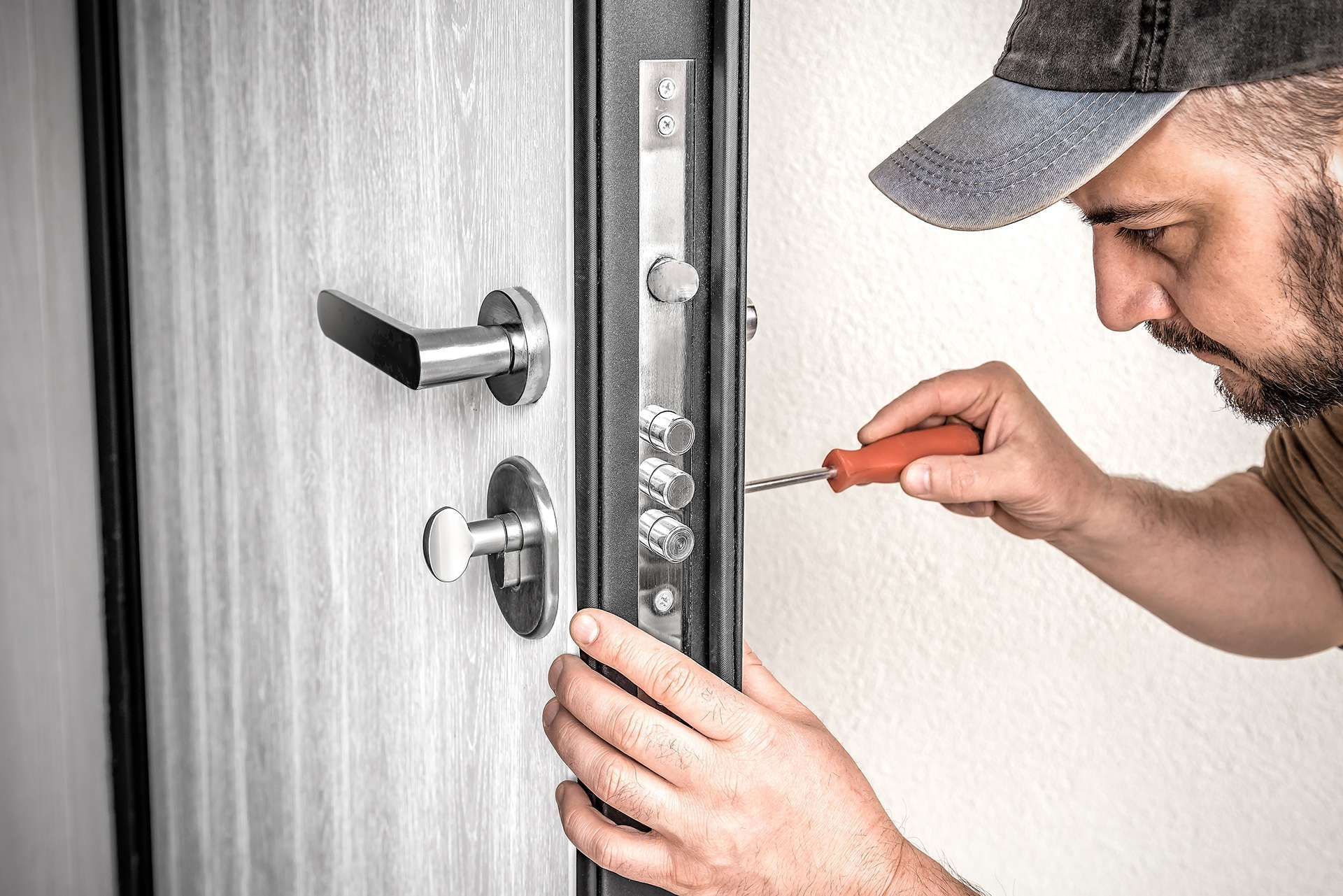 Handyman adjusting a door lock with a screwdriver on a gray door