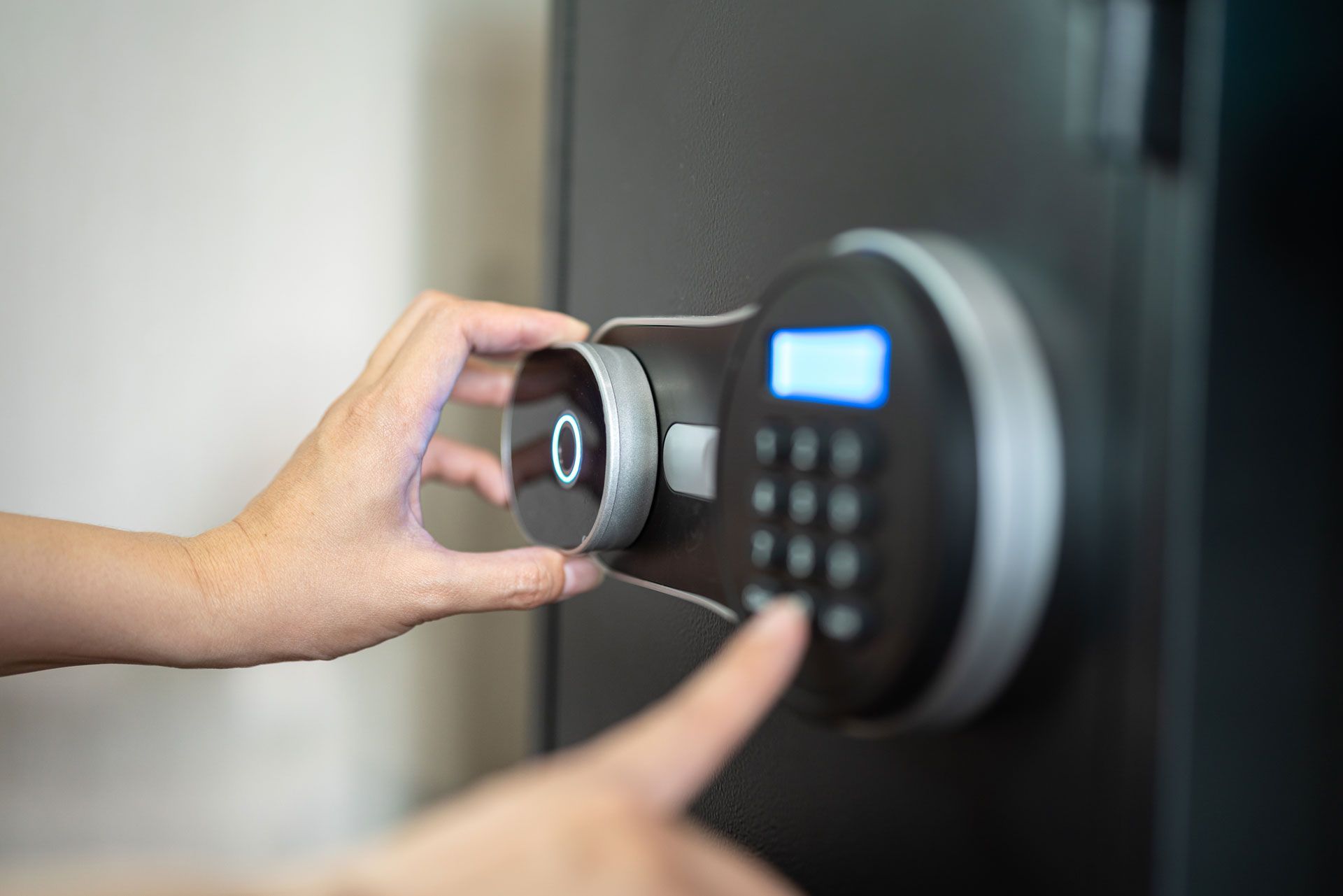 Hand holding a fingerprint scanner on a digital door lock with a keypad and blue display
