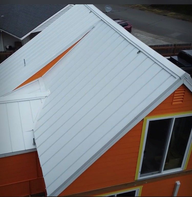 White metal roof on an orange house with white trim and a window.