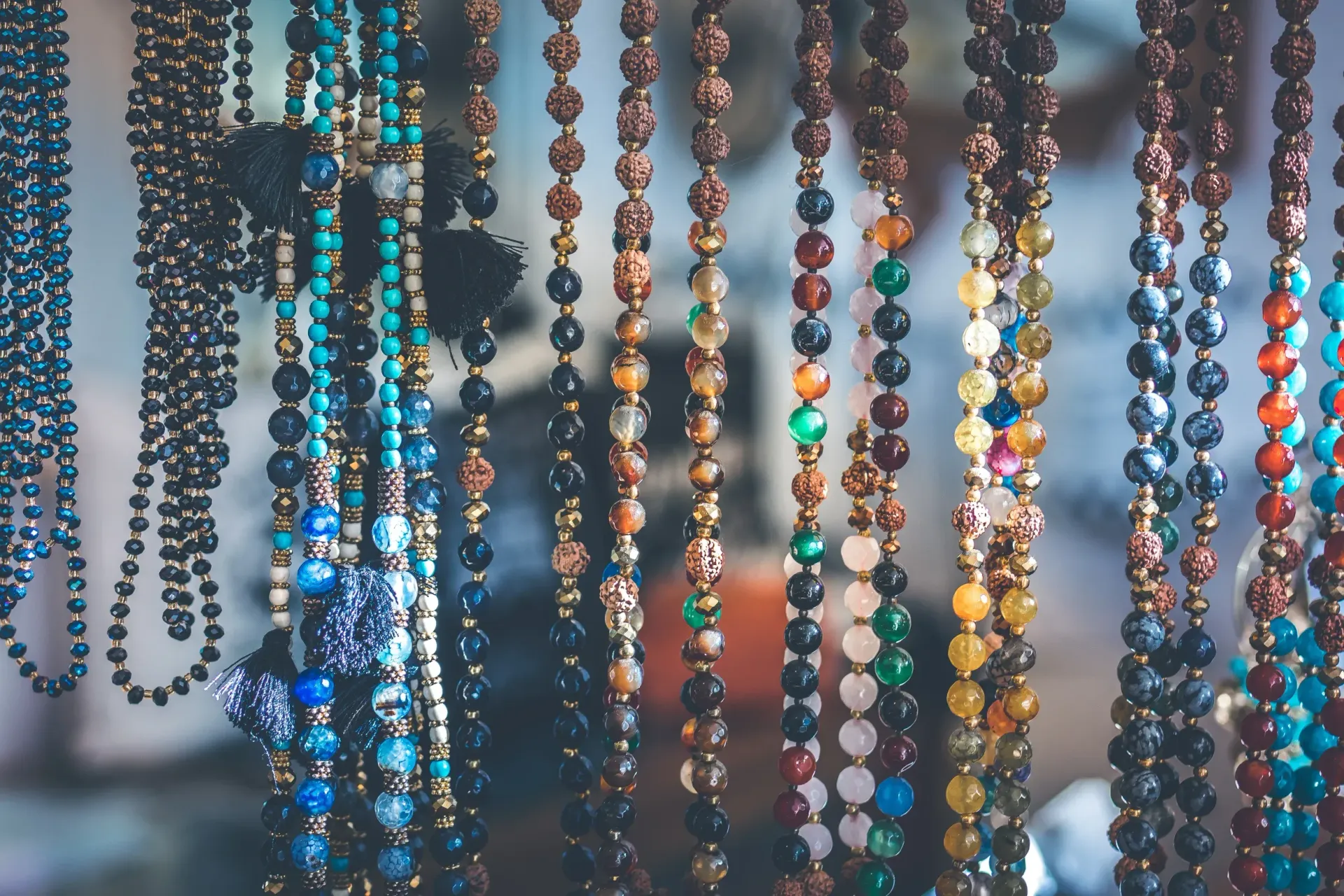 Colorful beaded strands hanging in front of a blurred background, with blue, pink, and brown beads