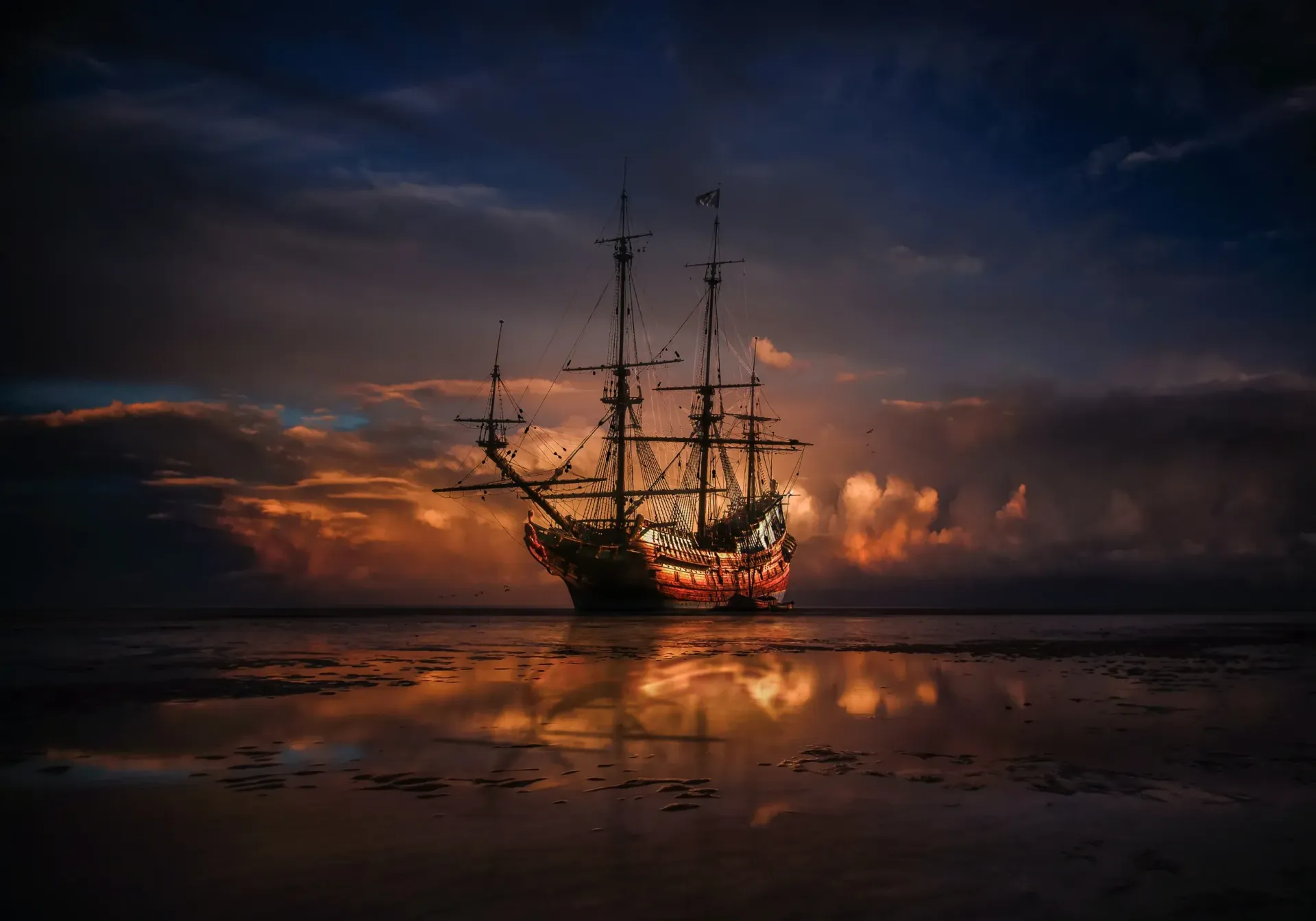 Tall sailing ship silhouetted at sunset on a calm, reflective sea
