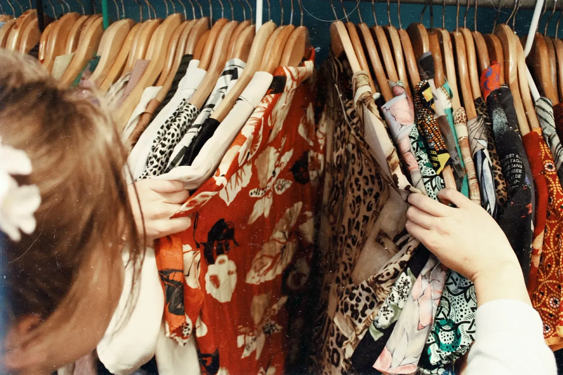 Hands browsing patterned dresses on a clothing rack in a boutique