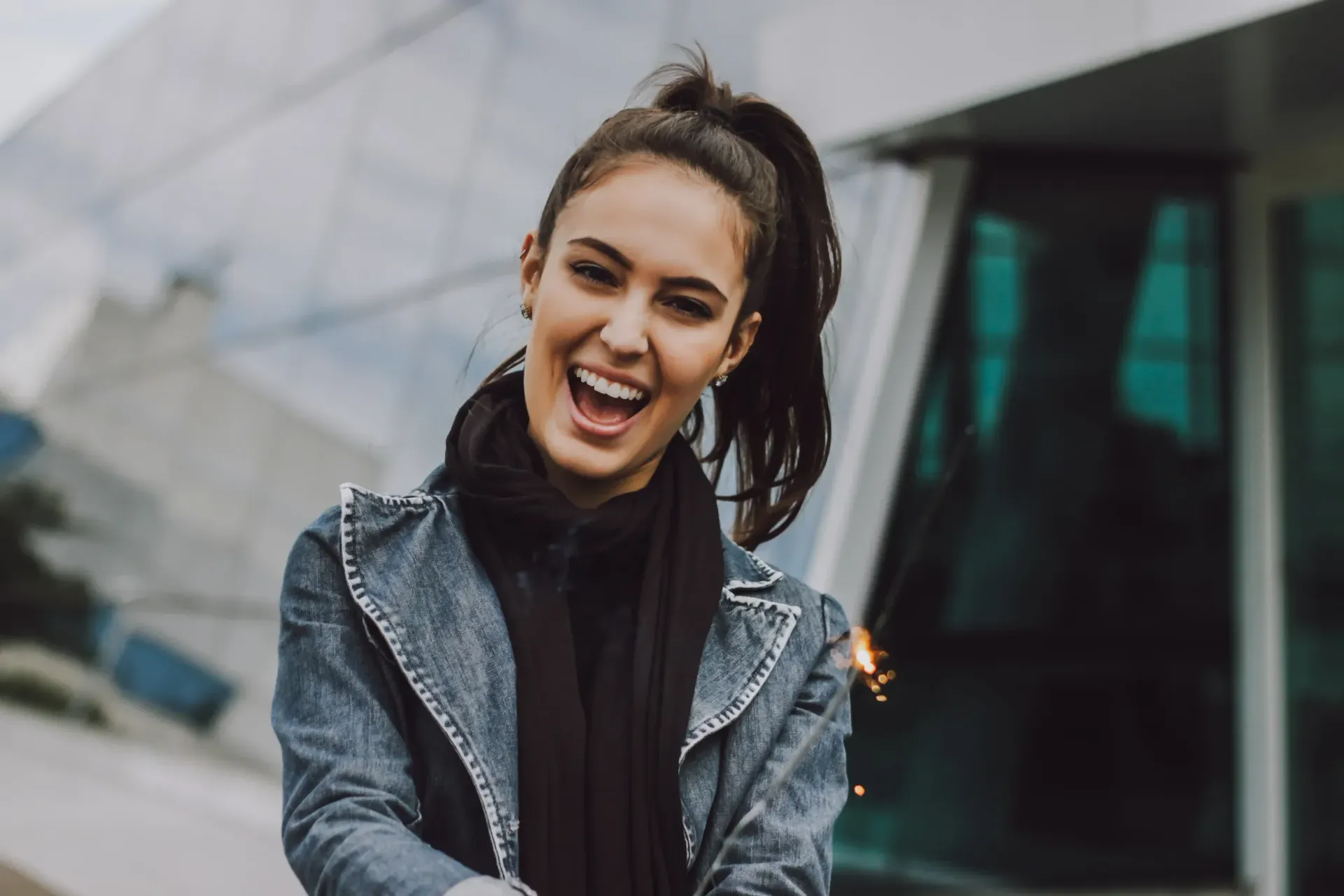 Smiling woman in a gray jacket standing outdoors by a modern building