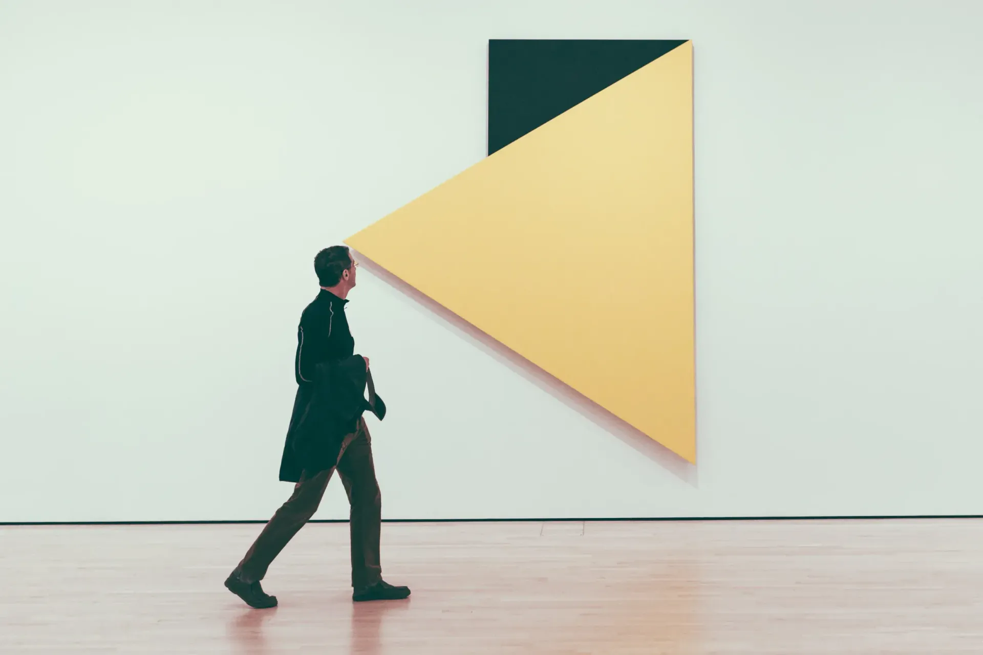 Person walking past a wall-mounted yellow triangular sculpture in a minimalist room