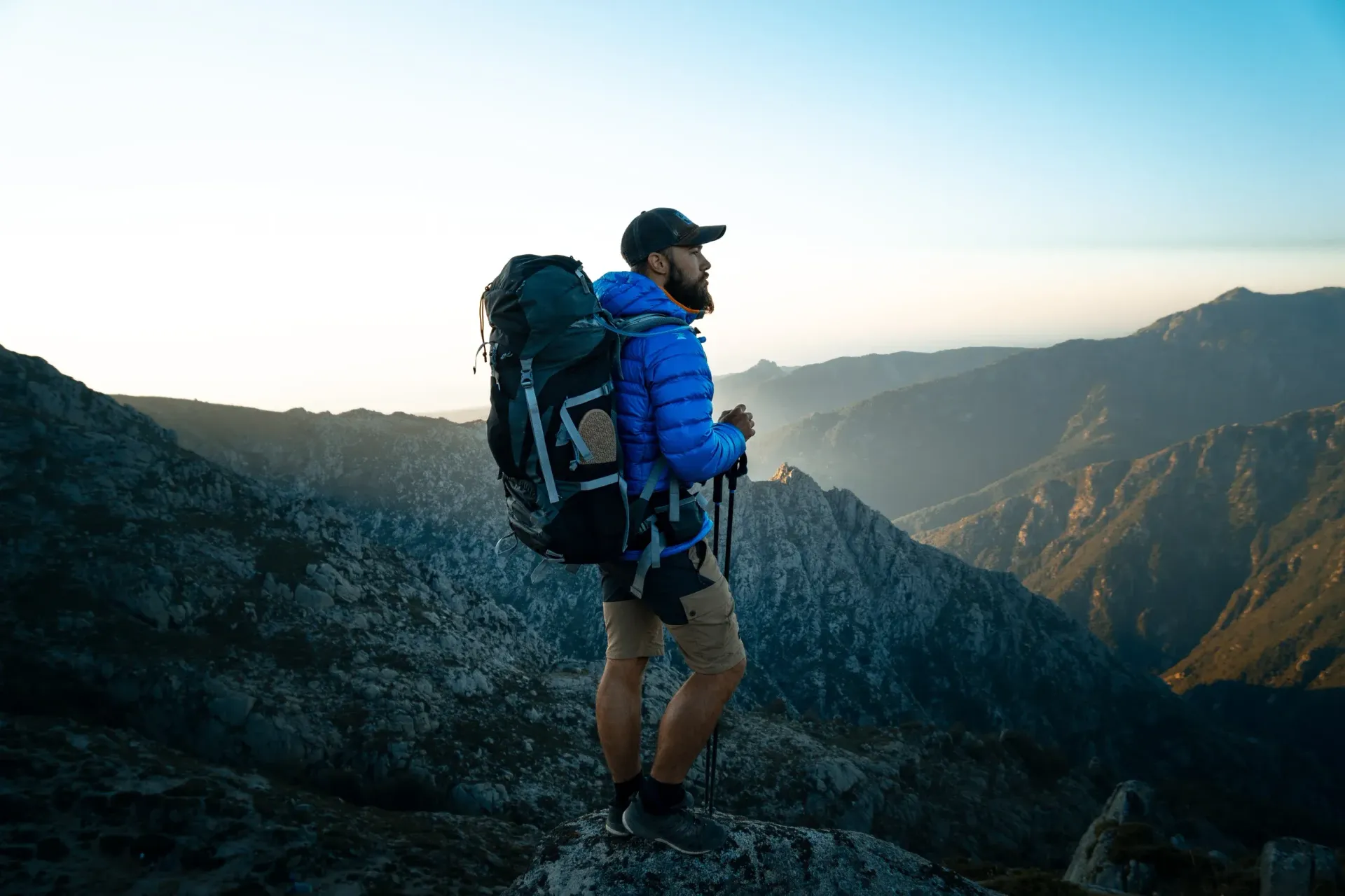 Hiker with backpack standing on a mountain ridge at sunrise, overlooking valleys and distant peaks