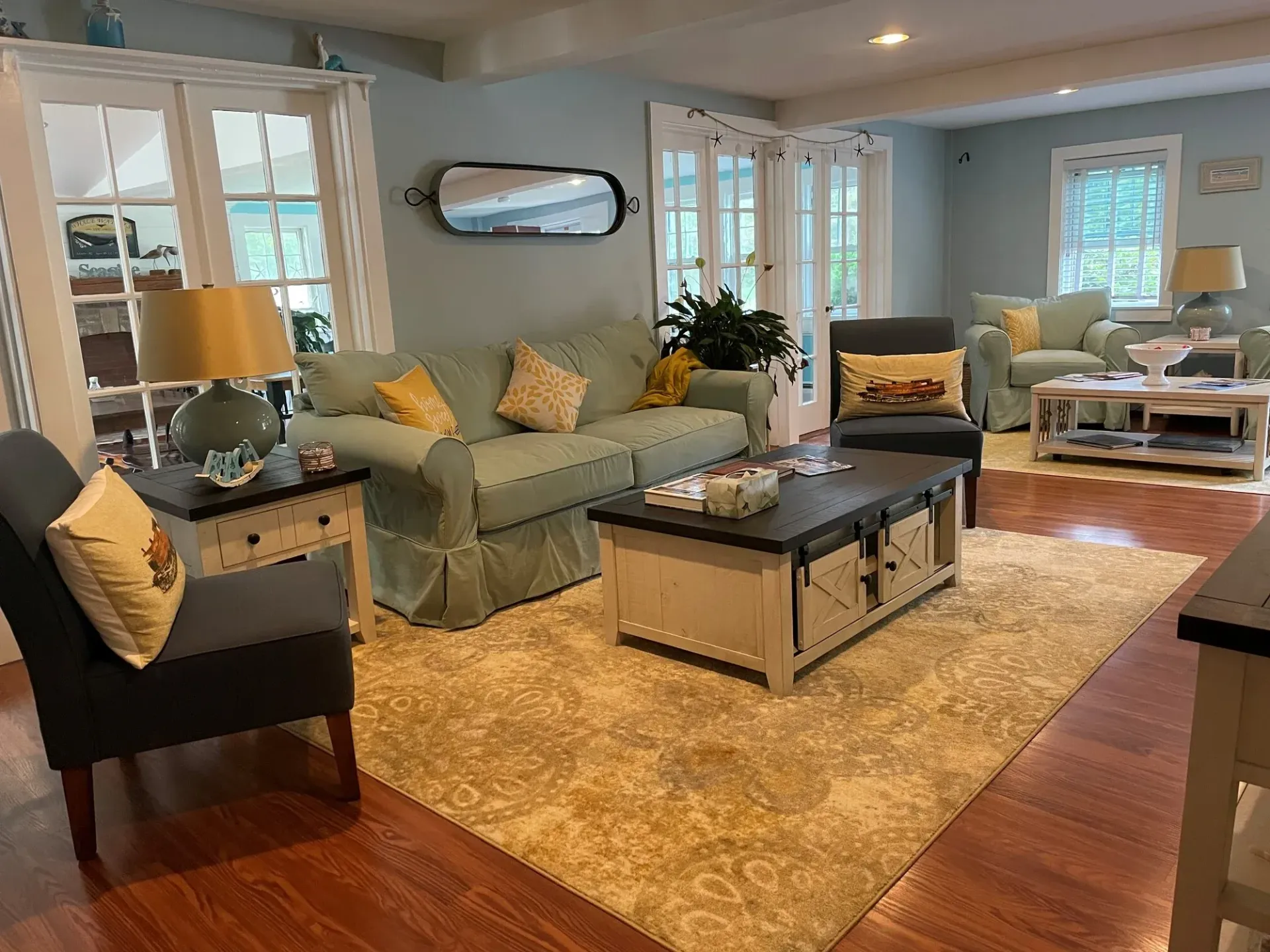 Bright living room with green sofas, tan rug, dark coffee table, and large windows letting in daylight
