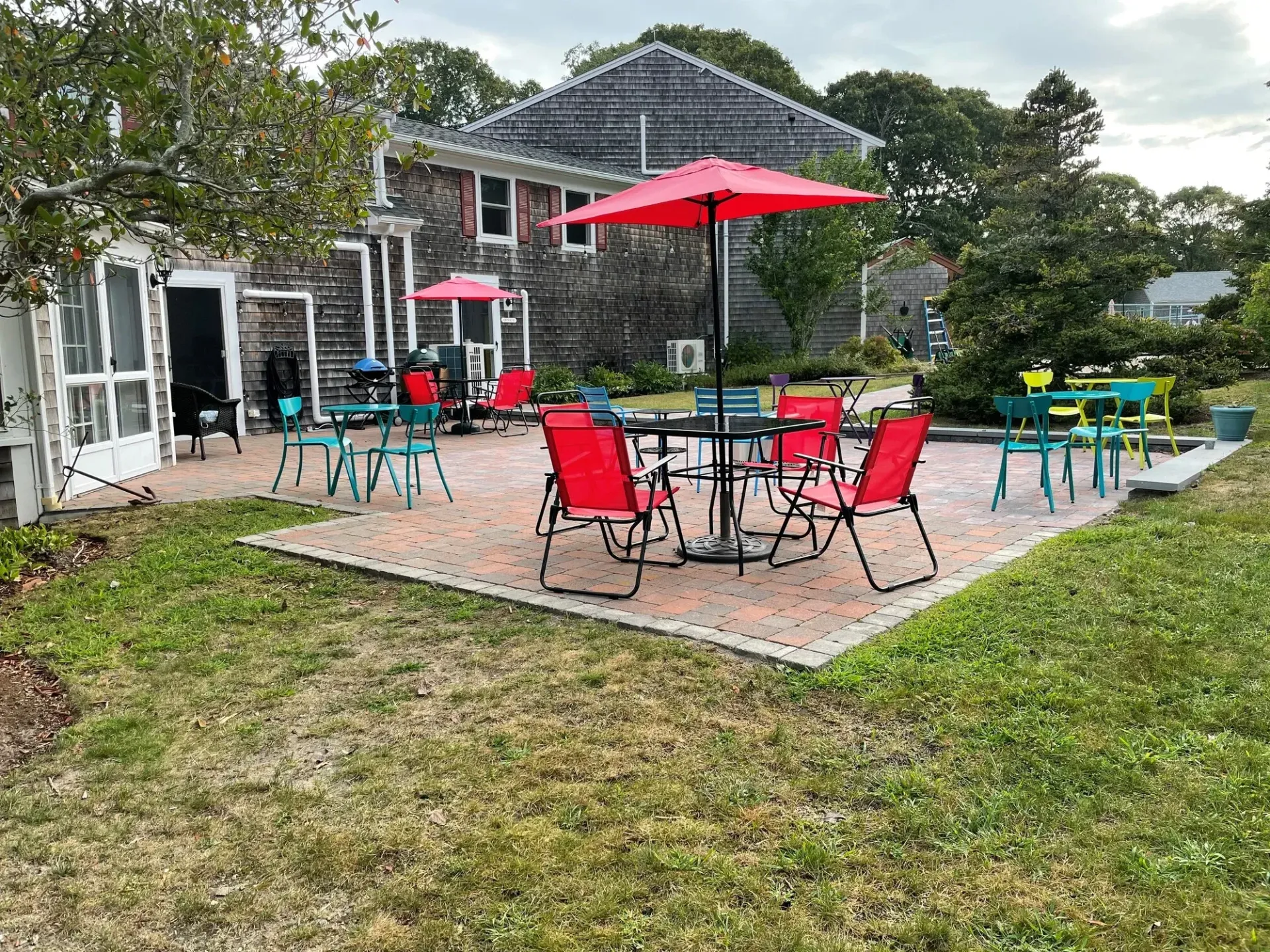 Patio with red umbrella and red chairs outside a house, surrounded by grass and trees