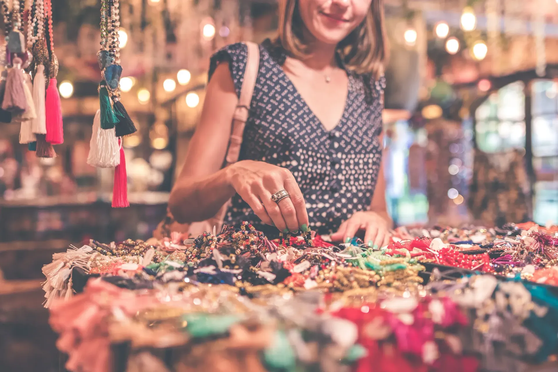 Woman browsing colorful jewelry at an outdoor market stall with sparkling lights