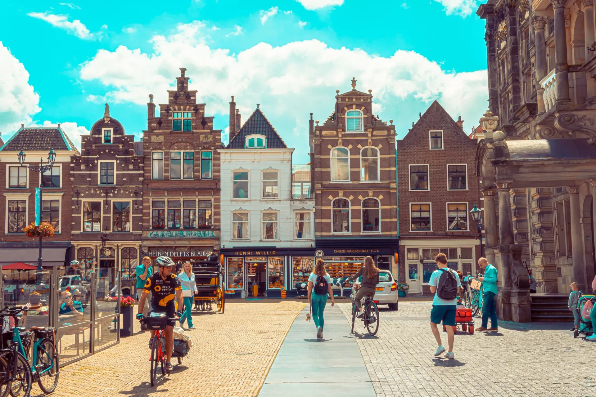 Historic European square with ornate brick buildings, people walking, and bicycles under a bright blue sky