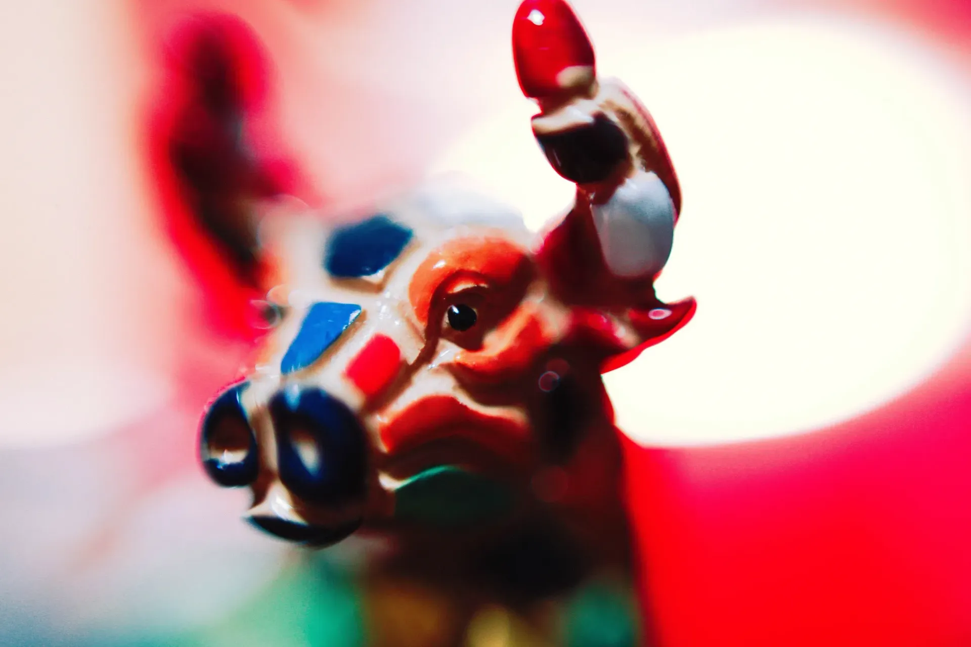 Close-up of a colorful toy cow figurine against a bright red and white blurred background