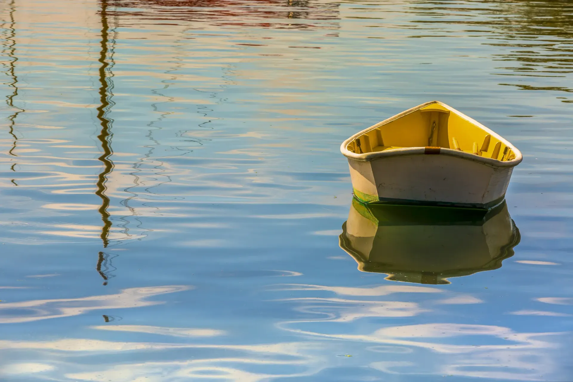 Small yellow boat floating on calm blue water with rippling reflections