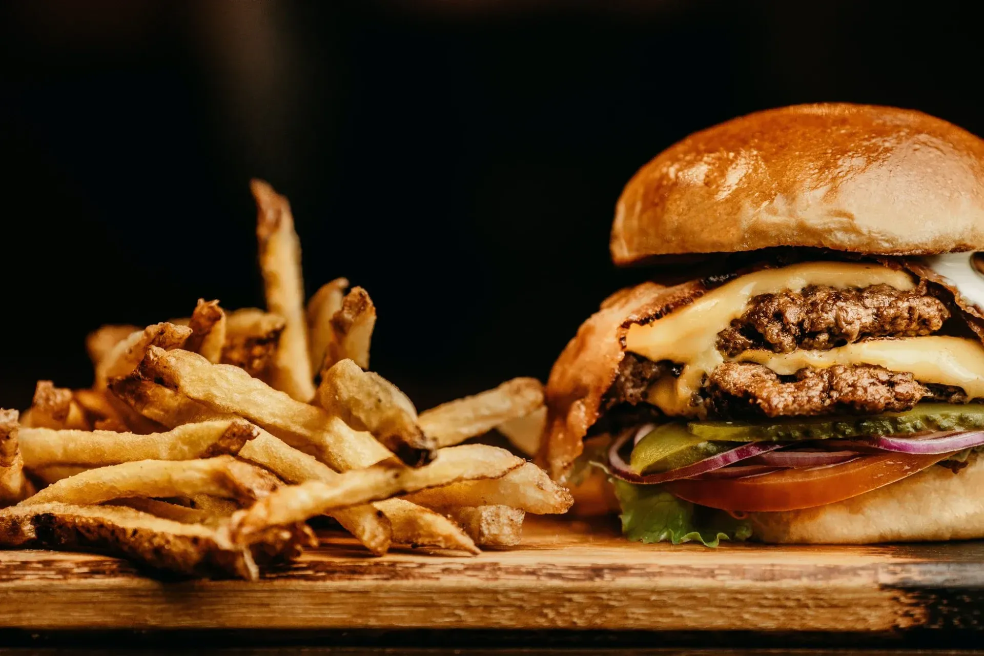 Burger with fries on a wooden board, with a sesame bun and dark background