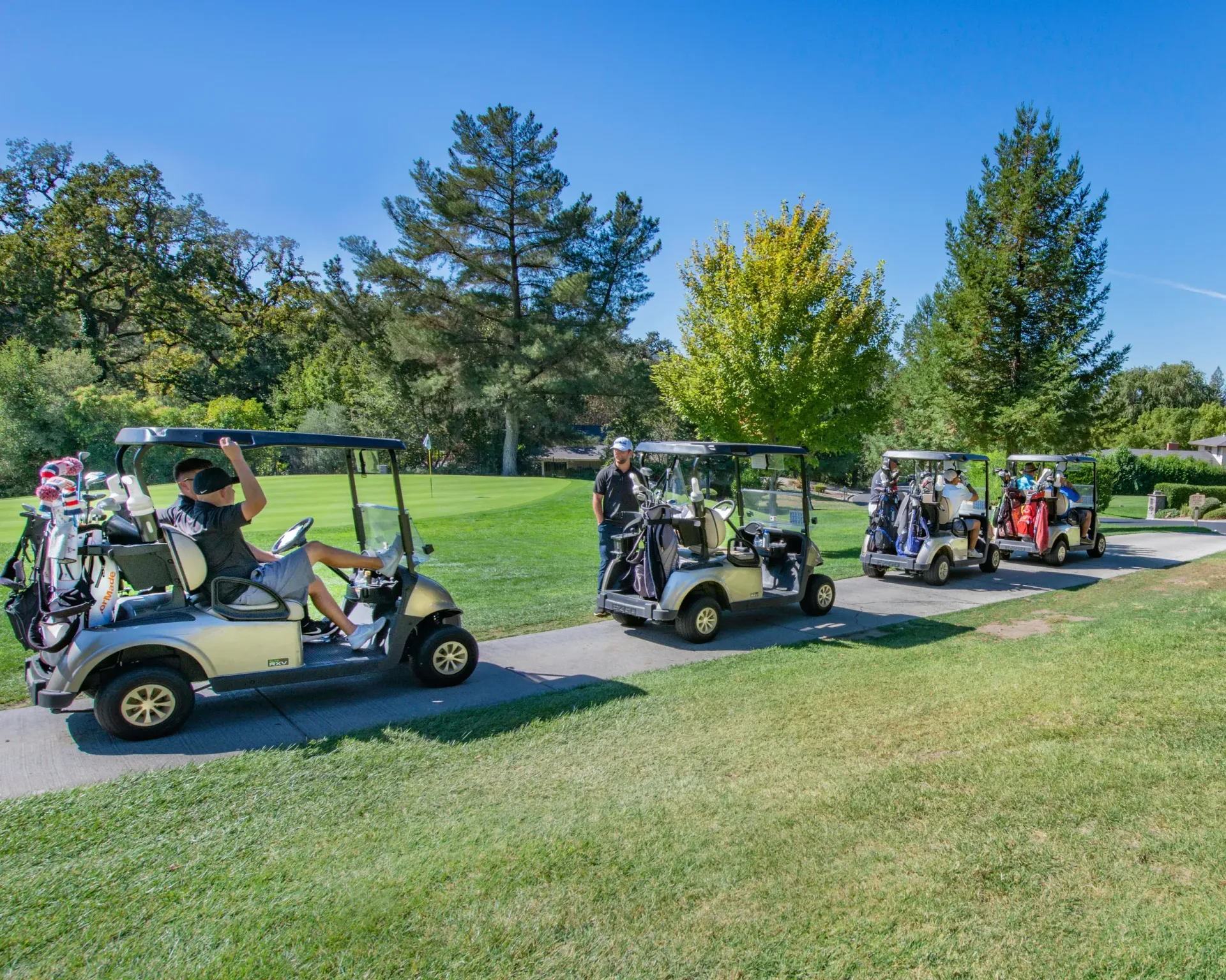 Golf carts lined up on a sunny golf course fairway with people seated inside.