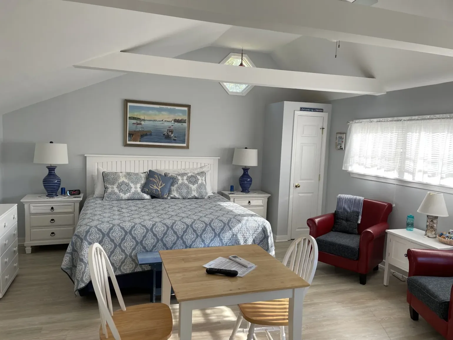 Bright bedroom with a bed, dresser, white chairs, red armchairs, and a skylight ceiling