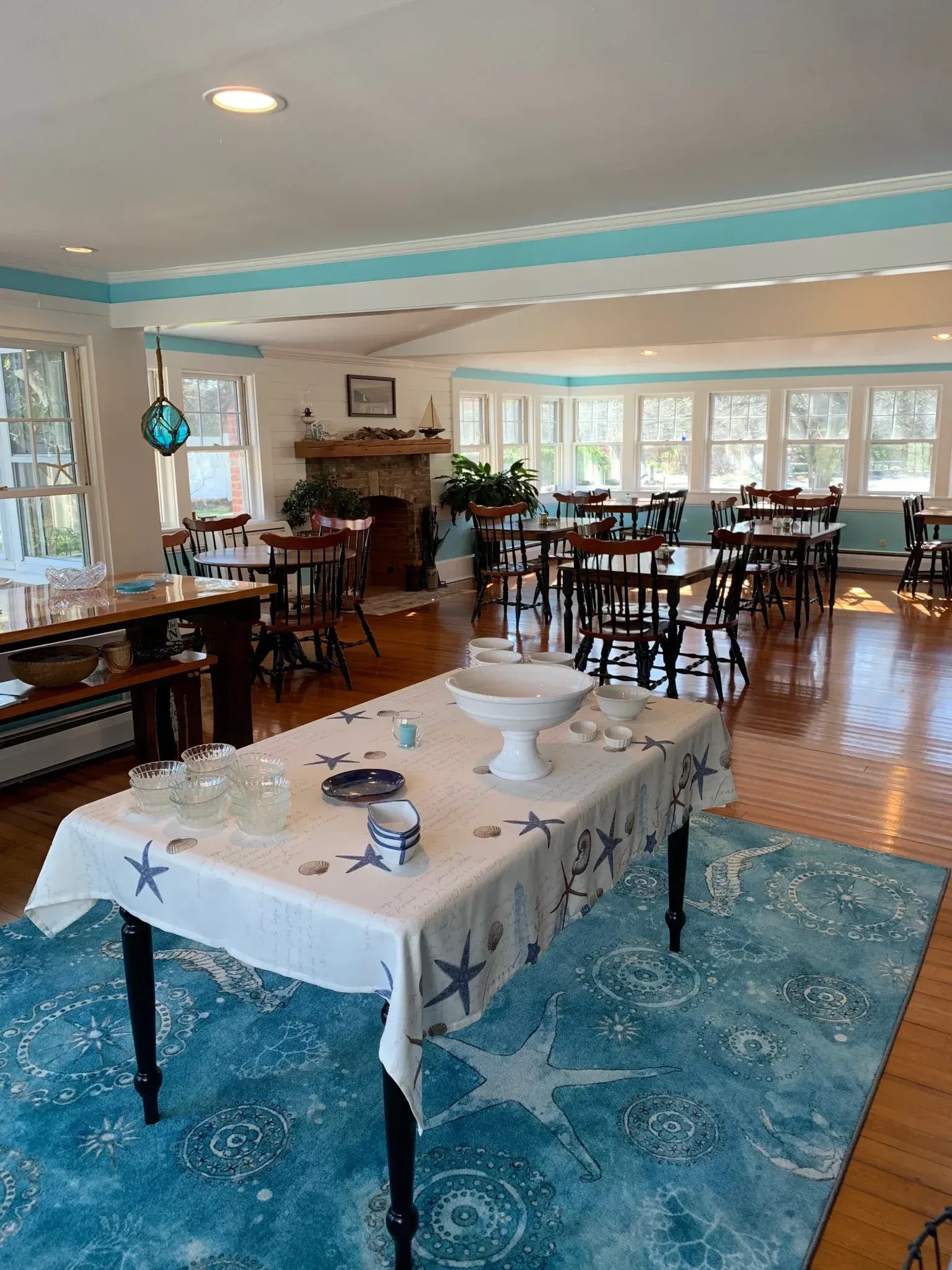 Bright dining room with long tables, white tablecloths, blue decor, and large windows.