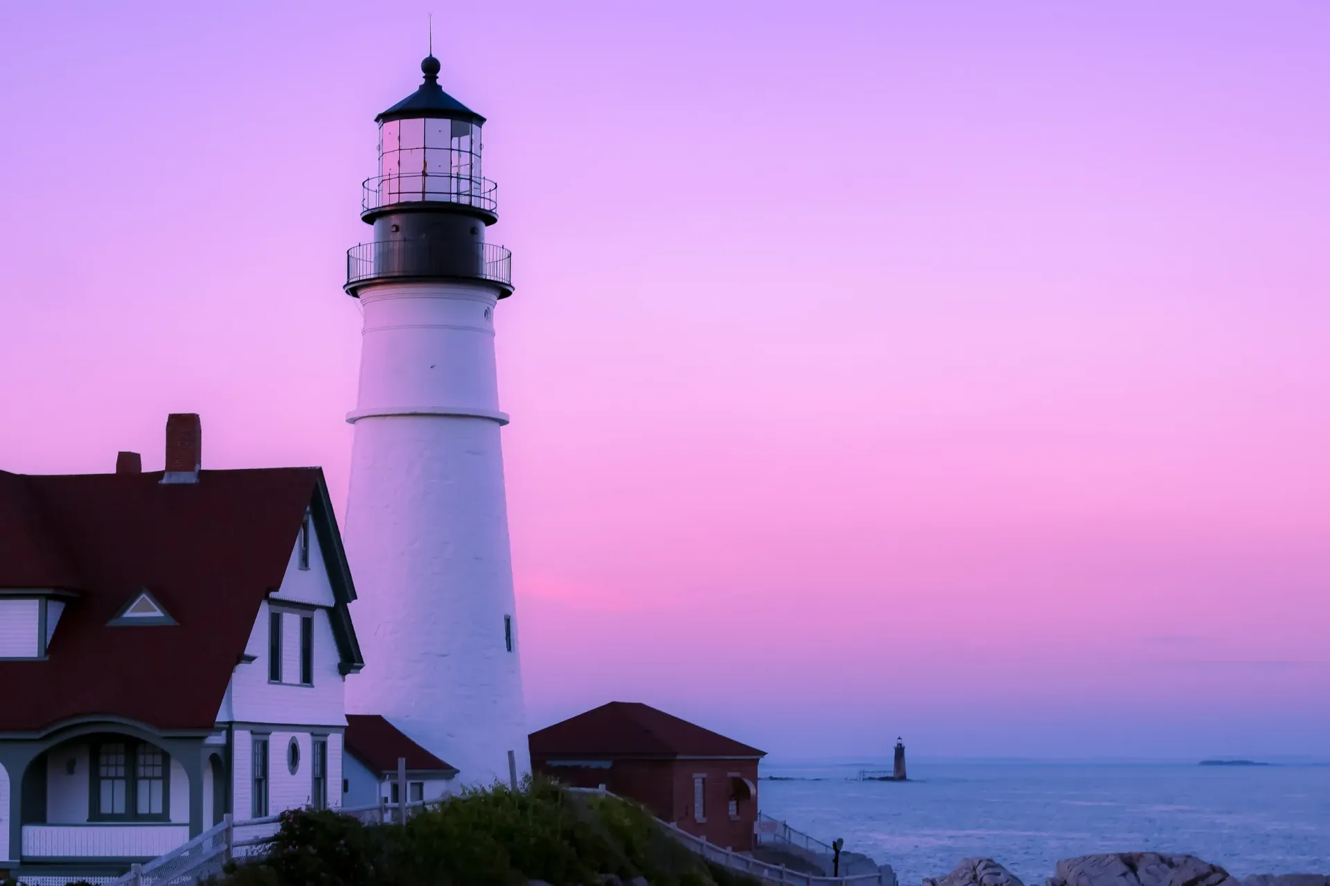 Lighthouse and seaside houses at dusk under a pink-purple sky