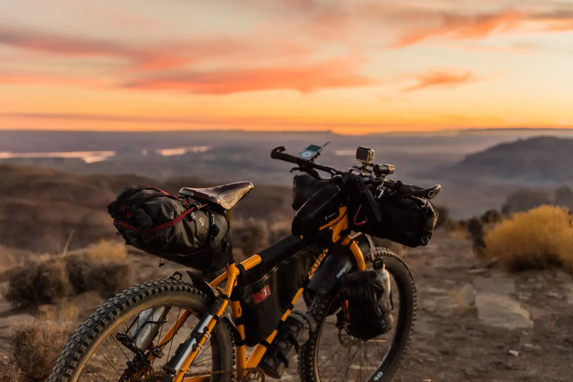 Loaded mountain bike on a dirt trail at sunrise, overlooking a misty valley with orange sky