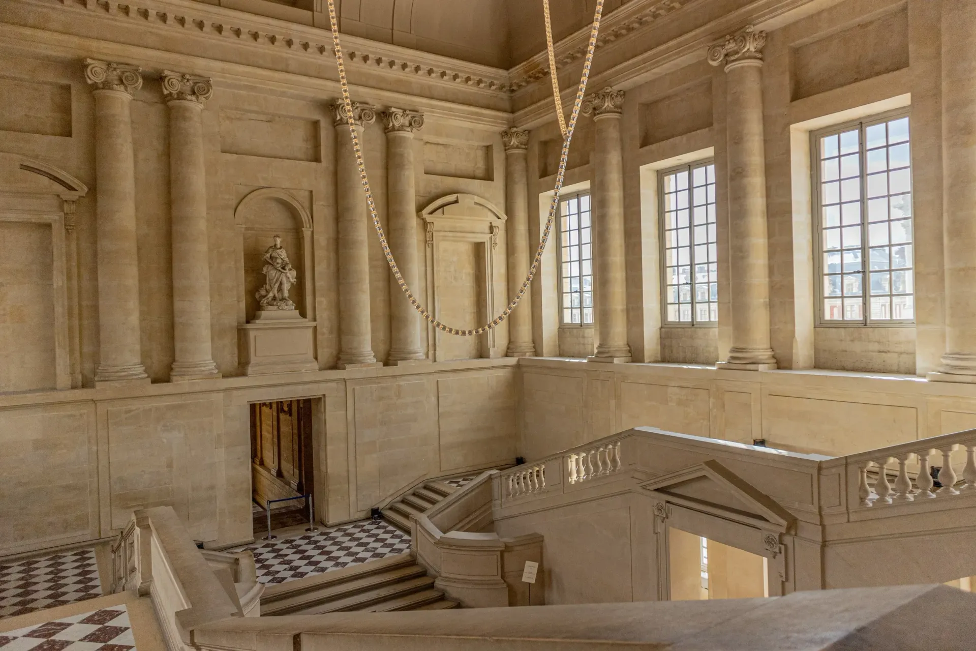Elegant beige grand hall with marble columns, ornate balcony, and tall sunlit windows