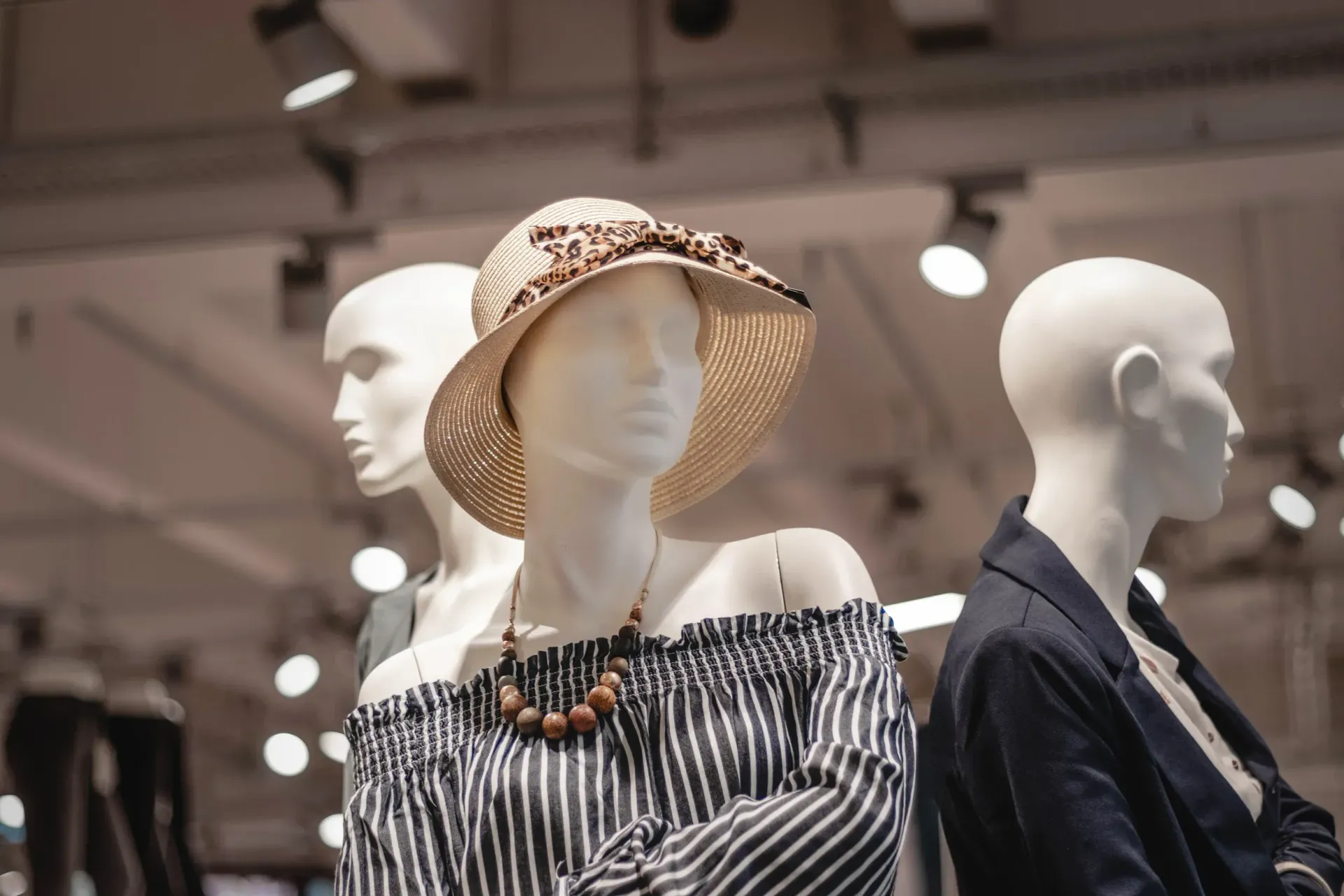 Mannequins in a clothing store display striped off-shoulder tops and hats under soft lighting