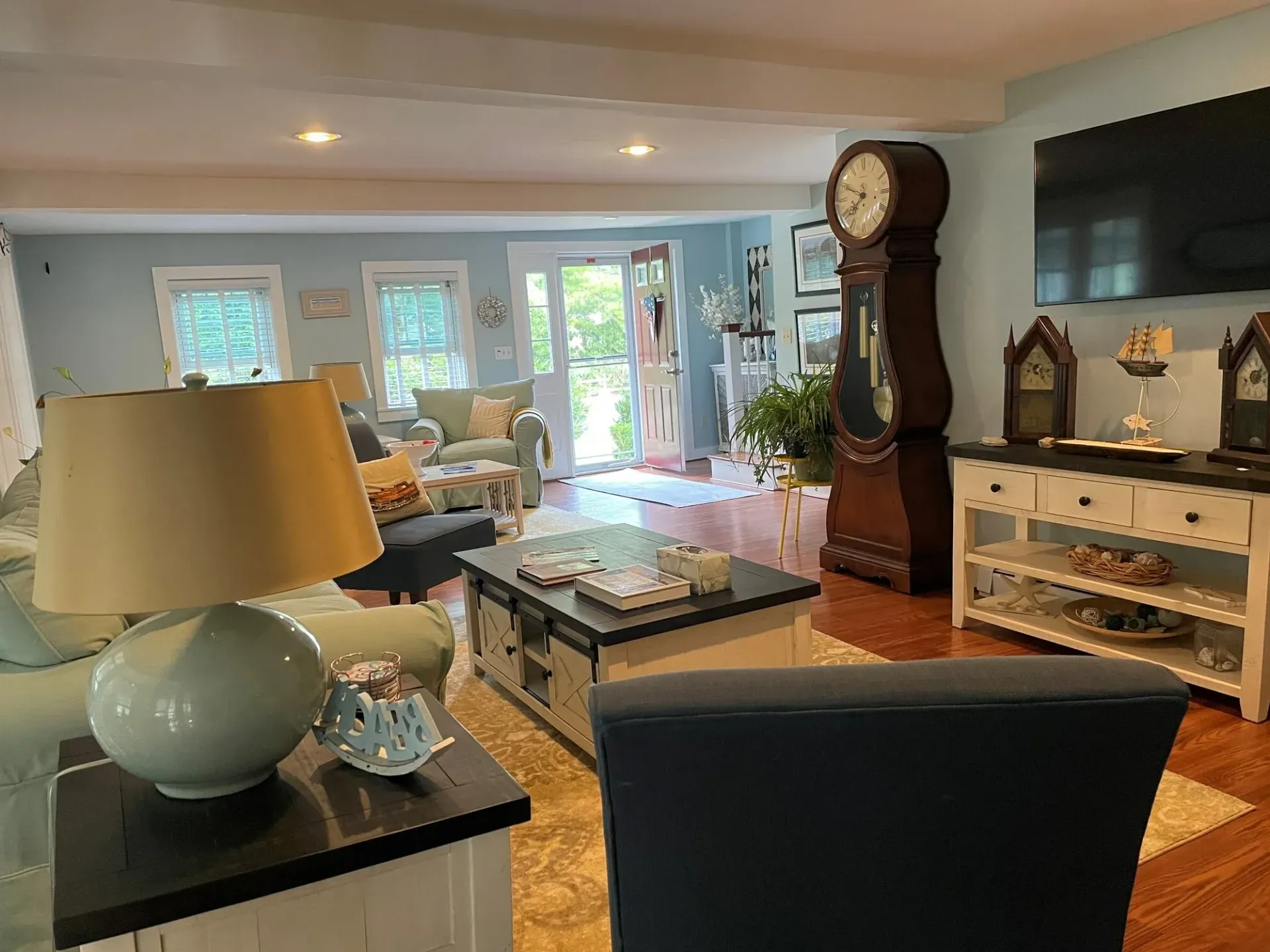 Bright living room with large windows, lamp, clock, and fireplace mantel in a cozy home interior.