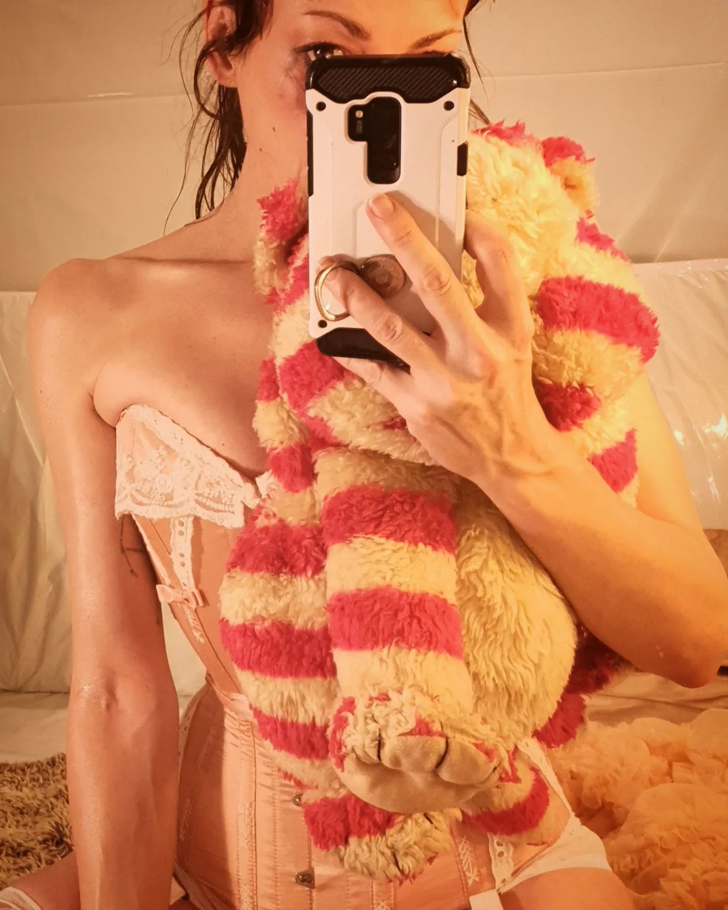 A woman in pink corset holding Bagpuss and looking over the top of her mobile phone. 