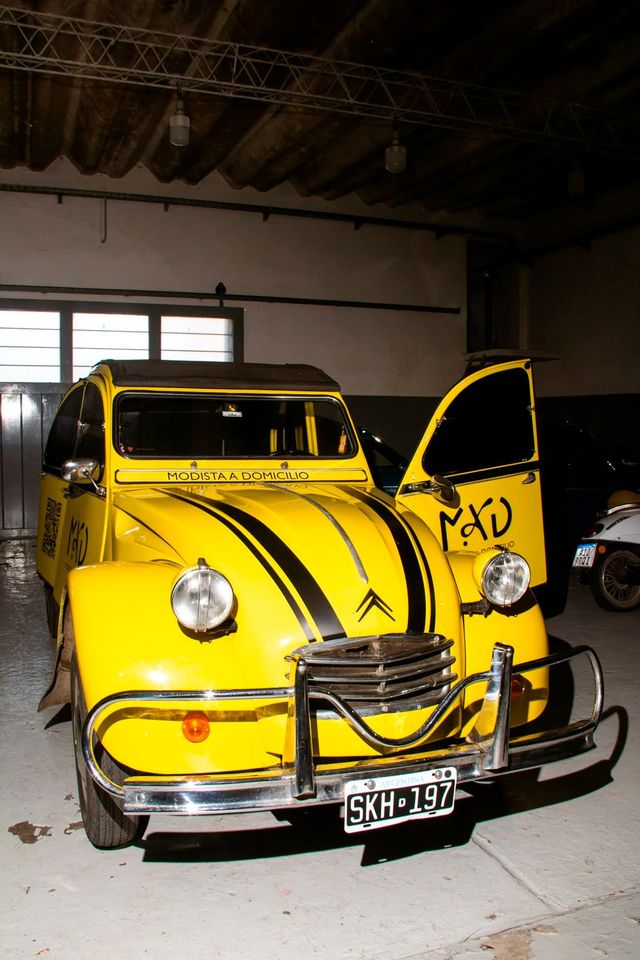 Un coche clásico de color amarillo brillante, con las puertas abiertas, aparcado en el interior de un garaje con poca luz.