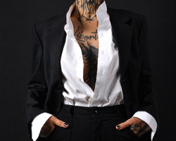 Persona con chaqueta de traje negra y camisa blanca, con las manos en los bolsillos y tatuajes visibles en el pecho.