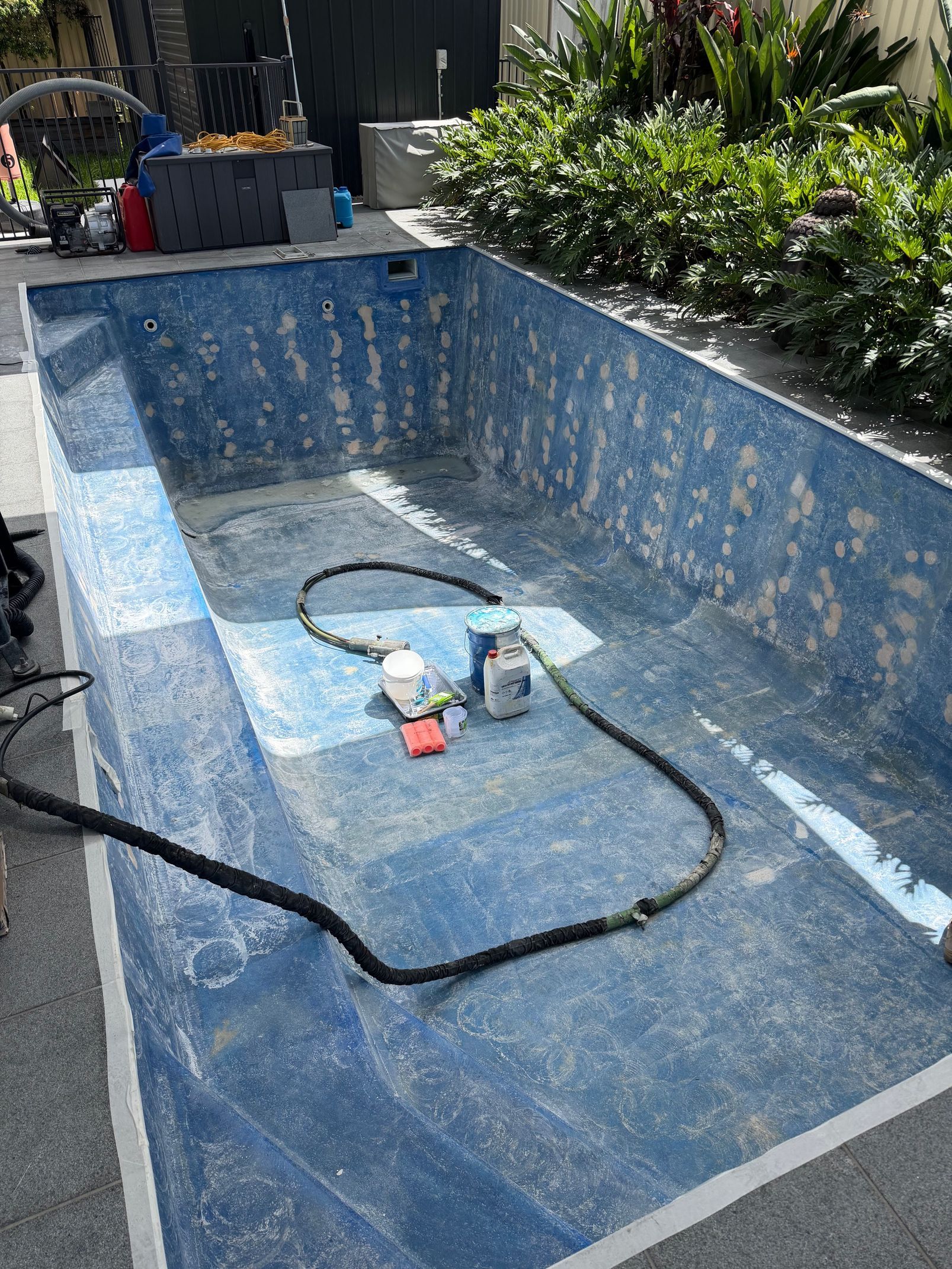 An empty rectangular swimming pool with blue speckled lining undergoing repairs, featuring a hose and equipment inside.  — East Coast Pool Resurfacing In Port Macquarie, NSW