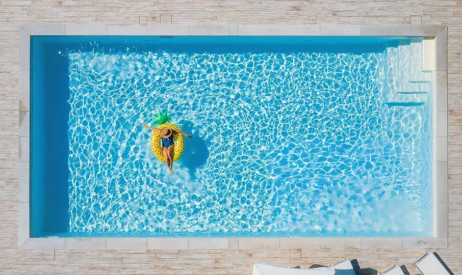 A person floating in a bright blue rectangular pool on a yellow pineapple-shaped inflatable ring. — East Coast Pool Resurfacing In Port Macquarie, NSW