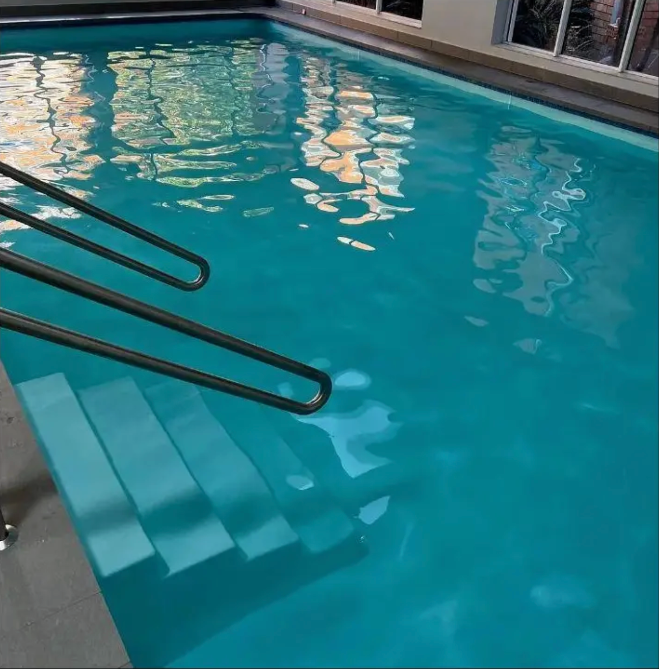Indoor swimming pool with turquoise water, featuring a set of stairs and metal handrails leading into the pool.  — East Coast Pool Resurfacing In Port Macquarie, NSW