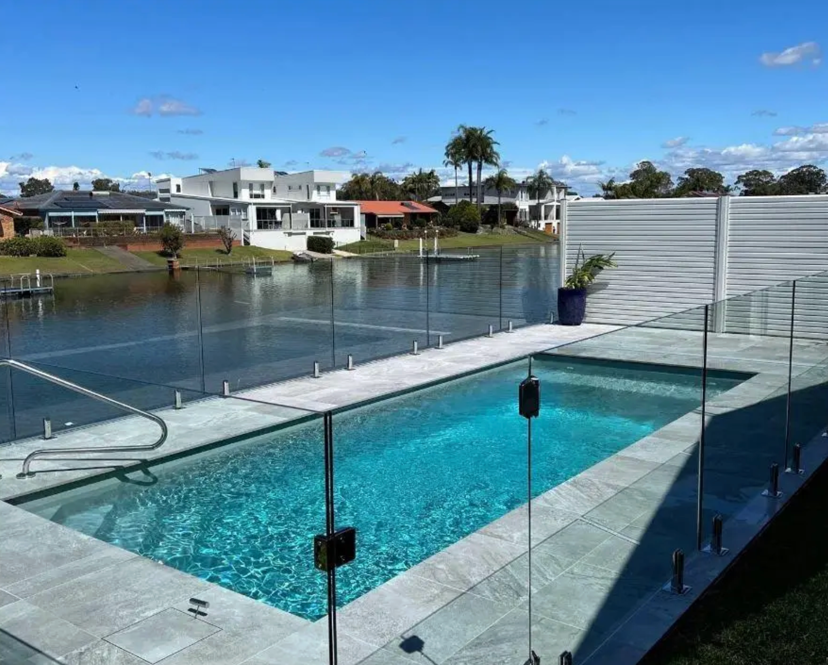 A rectangular turquoise swimming pool on a stone patio overlooking a canal with houses on the opposite shore. — East Coast Pool Resurfacing In Port Macquarie, NSW