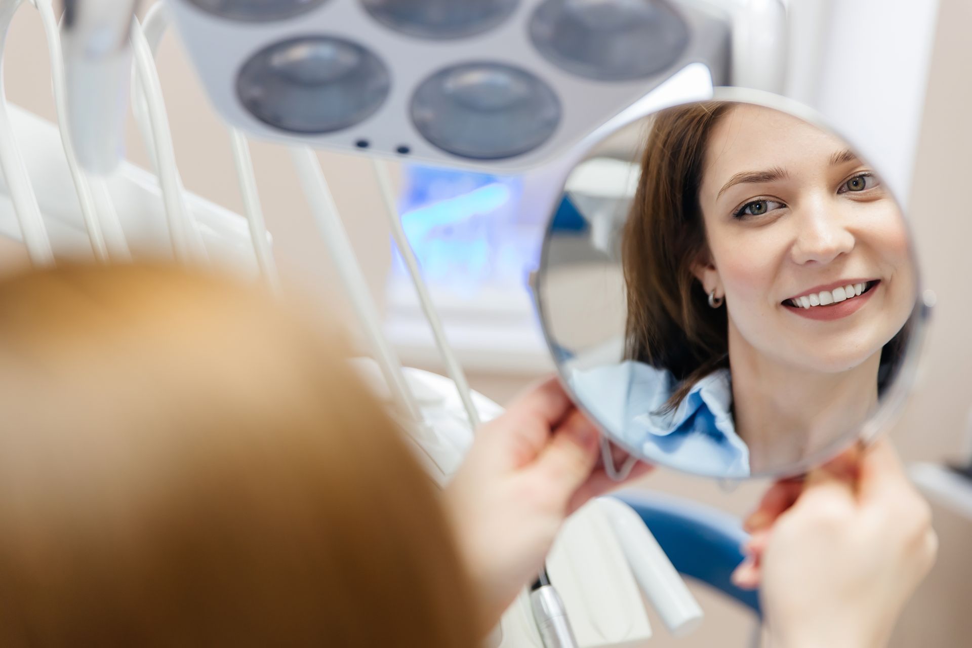 A person holding a handheld mirror to view their reflection in a dental office setting.