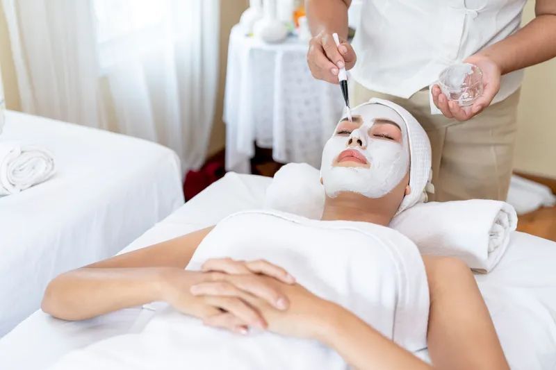 Woman receiving facial treatment with a light device, hands in gloves, warm light.