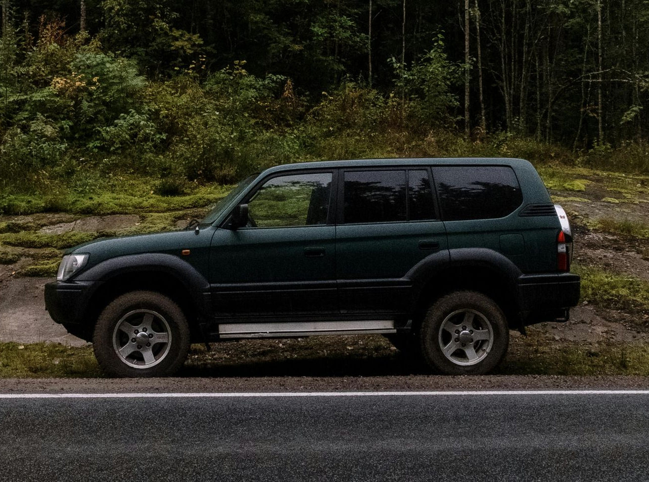 Dark green SUV parked next to a road with a wooded background.