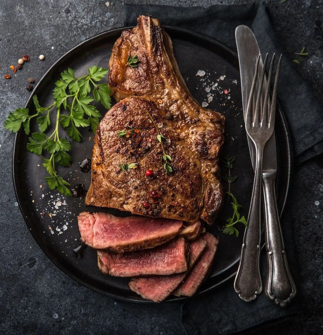 Seared steak with sliced medium-rare pieces on a dark plate, garnished with herbs and coarse salt.