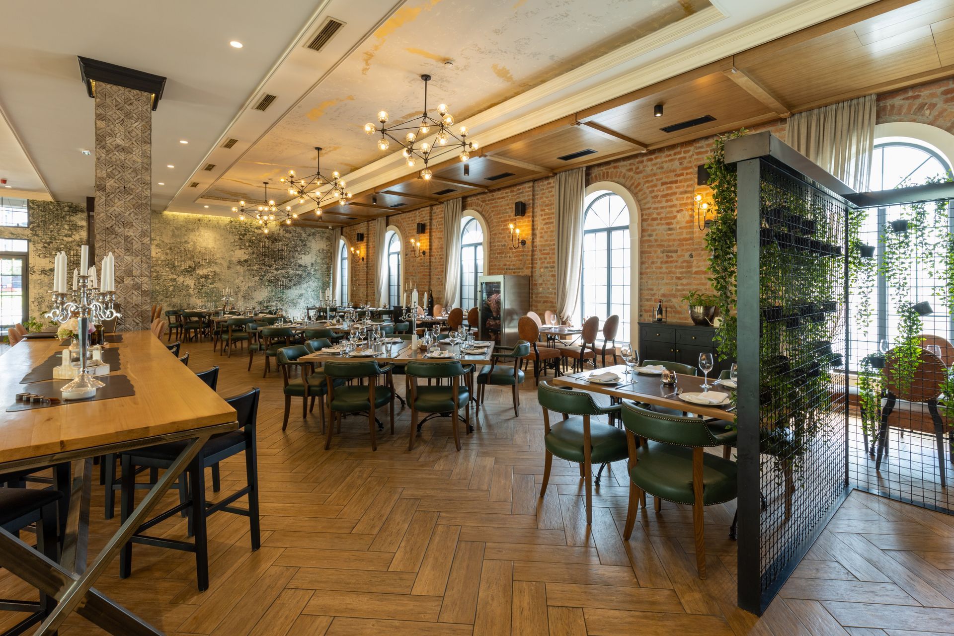 Elegant restaurant interior with wooden tables, green chairs, arched windows, and warm pendant lighting
